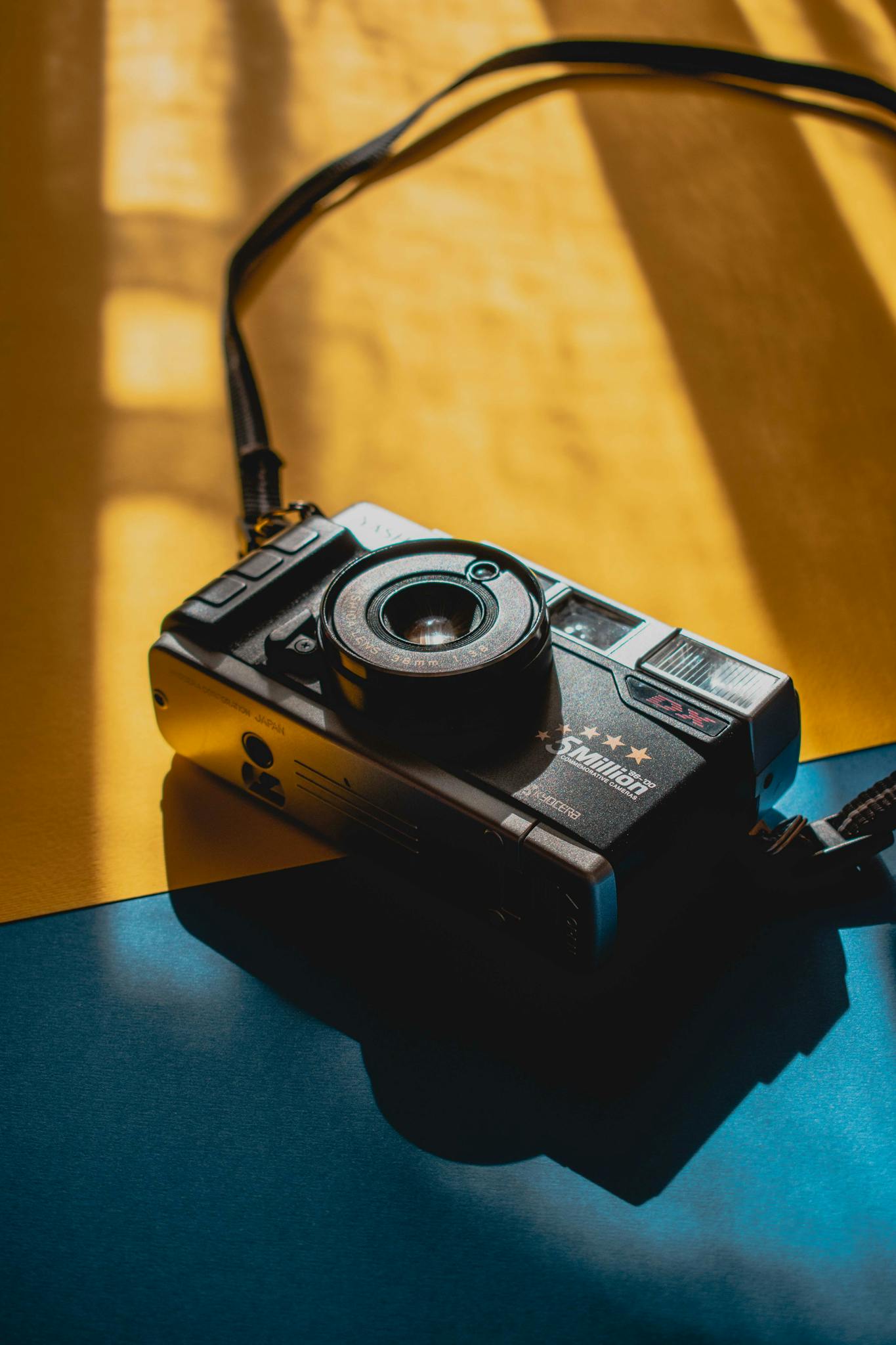 A vintage film camera placed on a vibrant blue and yellow background, with artistic lighting.